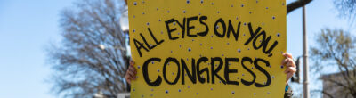 Activist with "All Eyes On You, Congress" sign